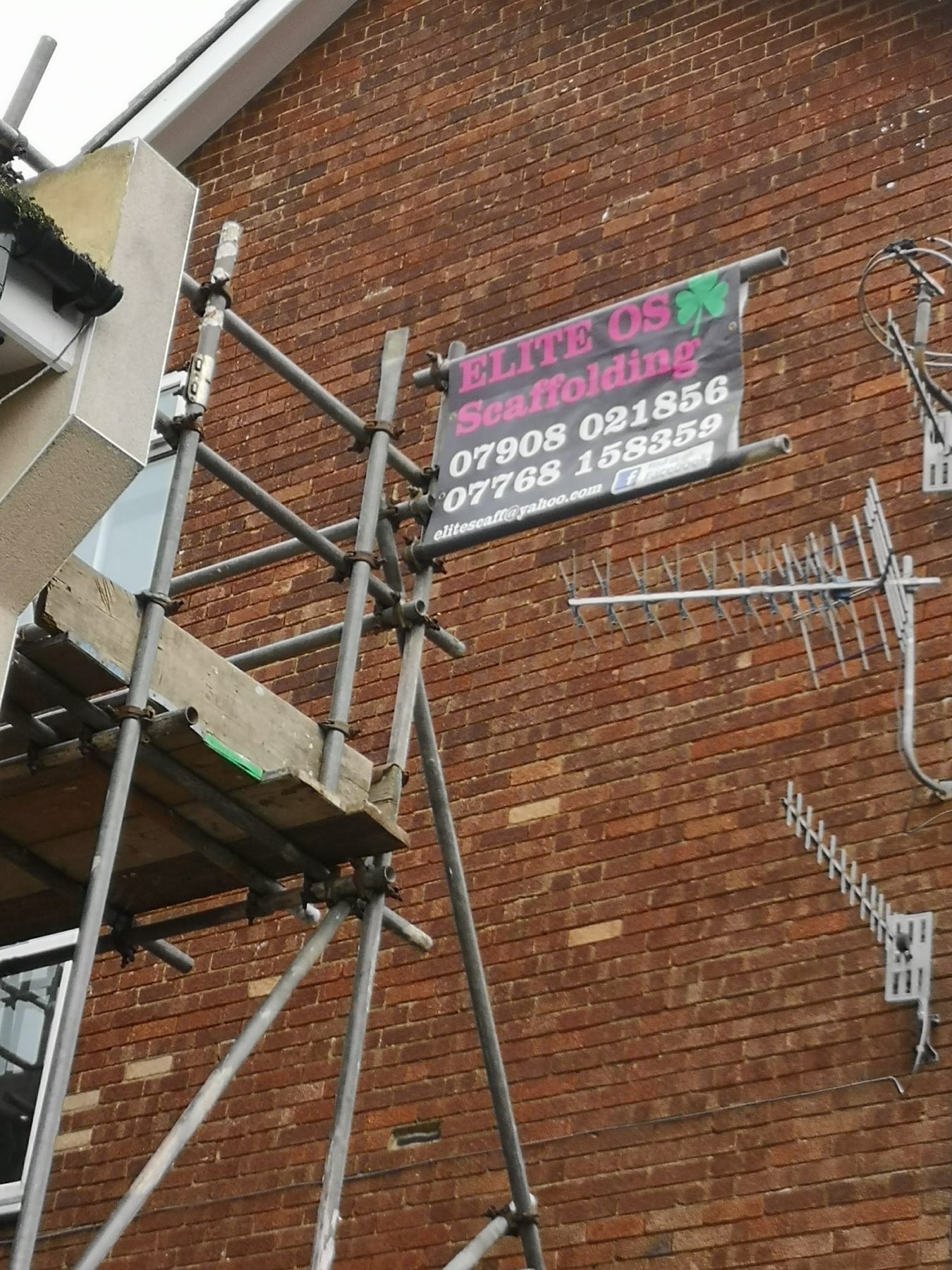 Elite Scaffolding site board fixed to scaffold tubes on a brick wall
