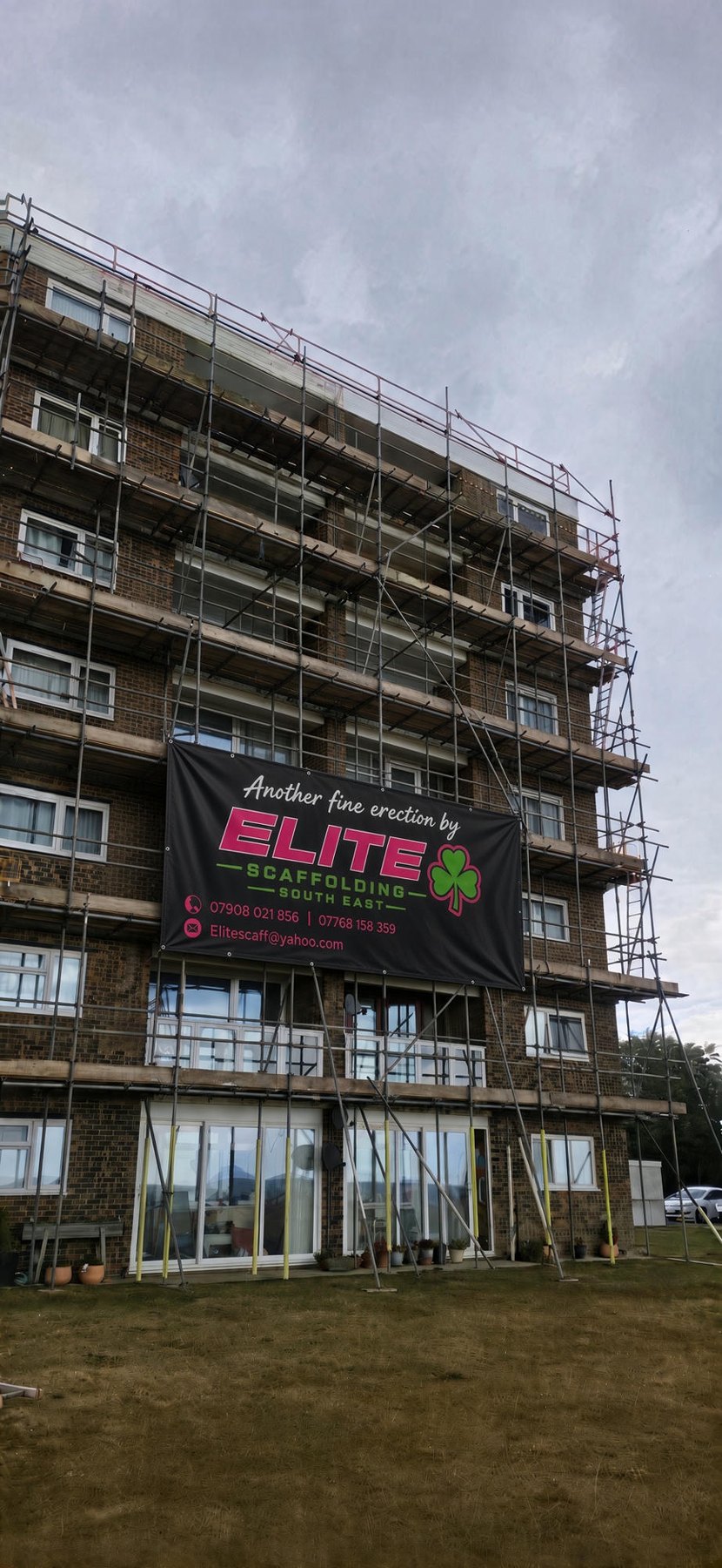 Full-height independent scaffold on a brick apartment block with an Elite banner