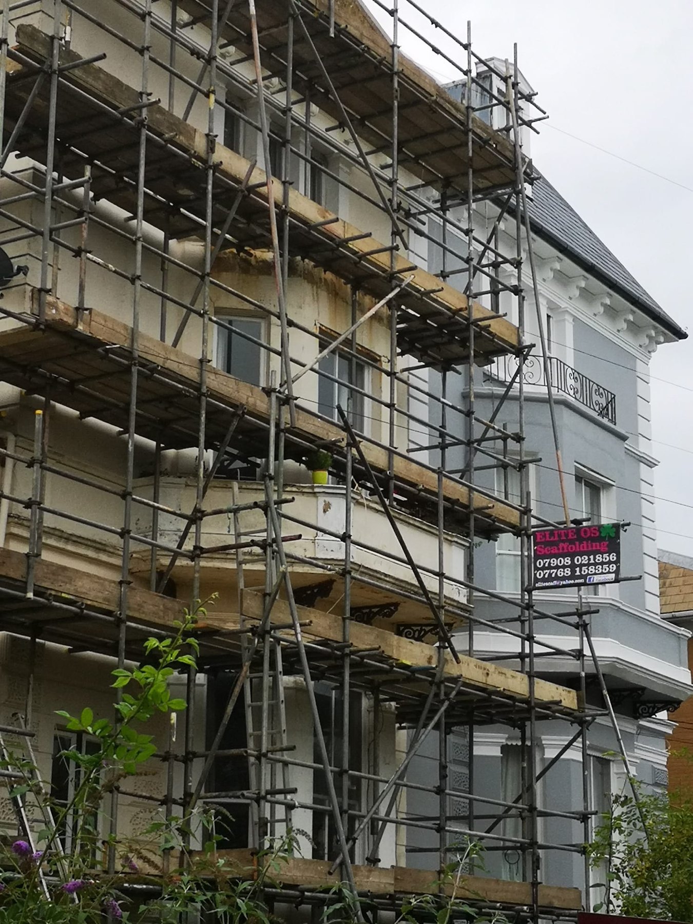 Scaffold on a grey and cream villa with a hanging Elite site board